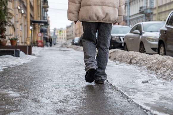 Person walking on slippery sidewalk rear view. Pavement covered with slippery ice. Frozen rain. Pedestrian walking on slippery sidewalk rear view. Pavement covered with slippery ice. Frozen rain. Wint ...