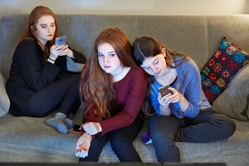 [Symbolic Image, Staged Picture, ] Sisters sitting on a couch in the living room use their smart phones while watching TV, photographed in Lucerne, Switzerland, on December 13, 2015. (KEYSTONE/Christo ...
