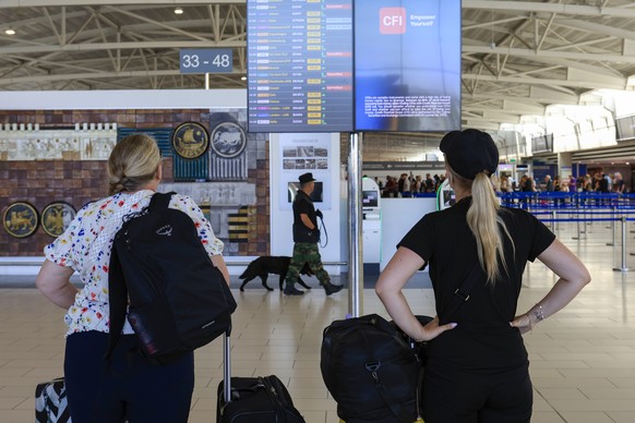 epa12187757 A member of Cyprus&#039; security forces walks with a sniffer dog past passengers looking at an electronic display showing cancelled flights from Israel at Larnaca International airport in ...