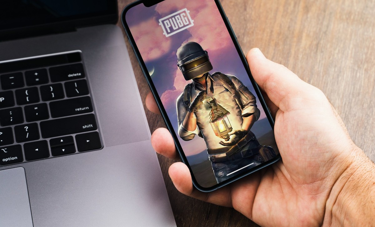 Male hand holding a smartphone with Player's Unknown Battleground, PUBG online shooting gaming mobile game app on the screen. Wooden Background. Rio de Janeiro, RJ, Brazil. August 2021.