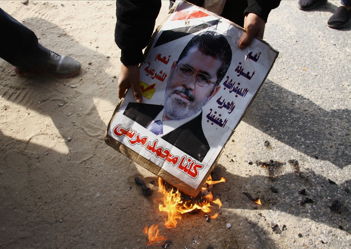 An opponent of Egypt's ousted President Mohammed Morsi burns a poster with his photo on it and Arabic that reads, "yes to bringing back democracy and true freedom, yes to legitimacy, we are  ...