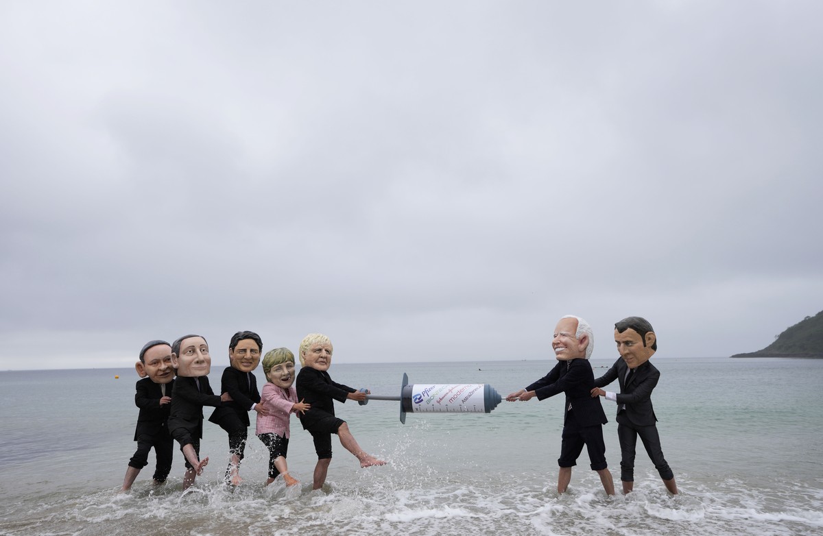 Activists wearing giant heads of the G7 leaders tussle over a giant COVID-19 vaccine syringe during an action of NGO's on Swanpool Beach in Falmouth, Cornwall, England, Friday, June 11, 2021. Lea ...
