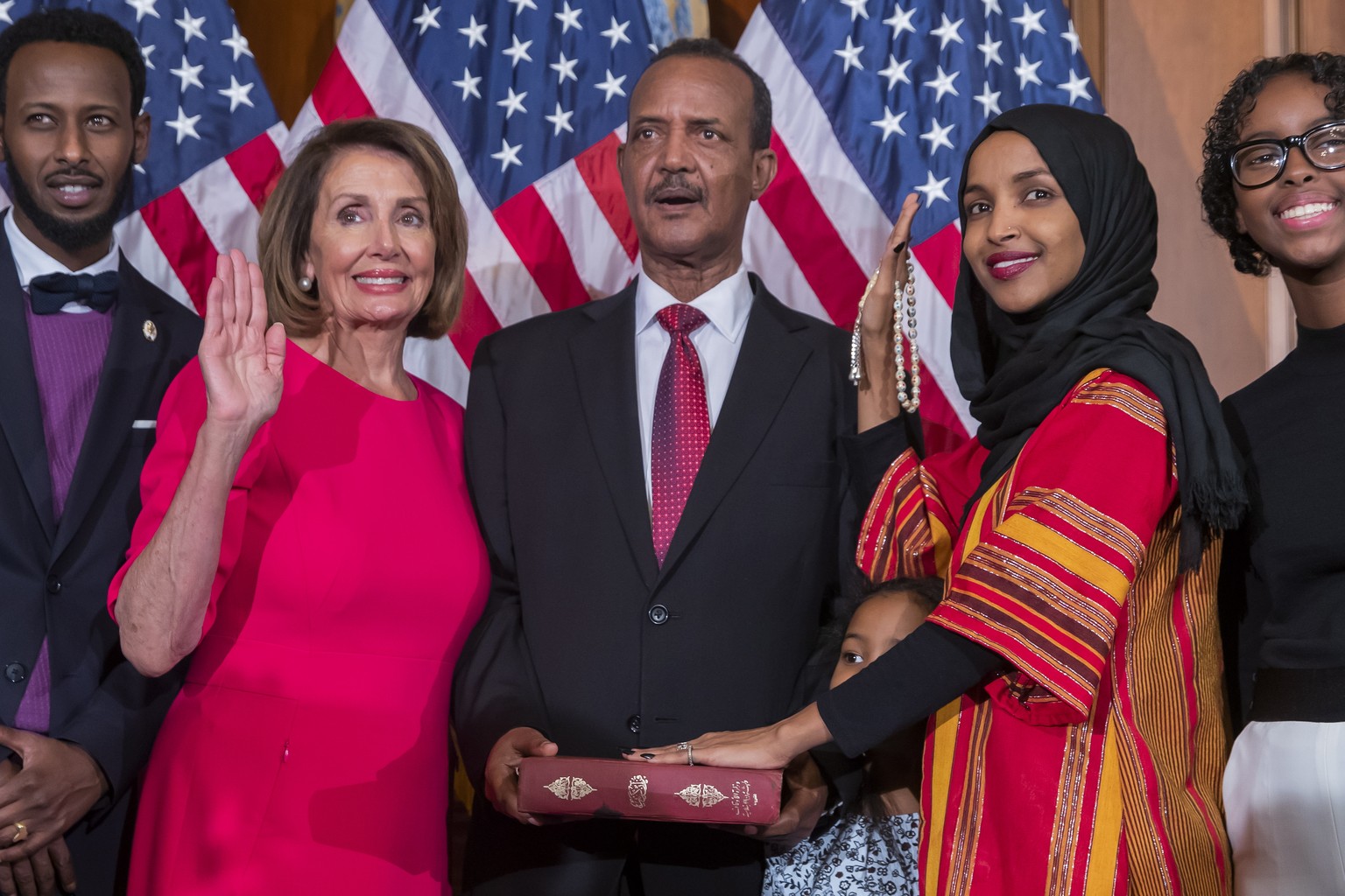 epa07260651 Democratic Representative from Minnesota Ilhan Omar (2-R), uses the Koran of her late grandfather while posing with new Democratic Speaker of the House Nancy Pelosi (2-L), during the first ...
