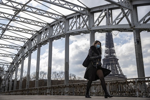 epa09083912 A pedestrian wearing a protective face mask walks across a footbridge near the Eiffel Tower in Paris, France 19 March 2021. French Prime Minister Castex announced on 18 March additional lo ...