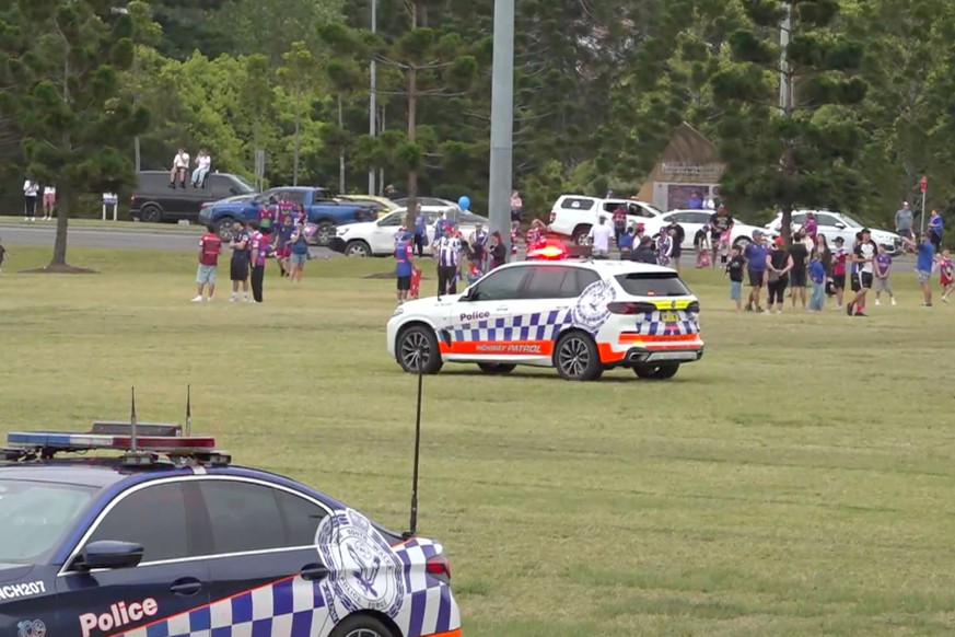 In this image made from video, emergency workers and pedestrians gather near the site where a car drove into a large crowd standing on a road near Newcastle, Australia, Saturday, Oct. 3, 2026. (Austra ...