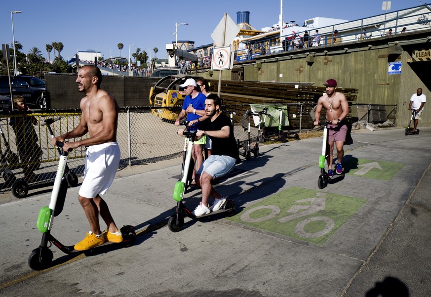 In this July 1, 2018 photo people ride Lime and Bird scooters along the strand in Santa Monica, Calif. The shared electric scooters could be banned in Los Angeles until regulations are approved and pe ...