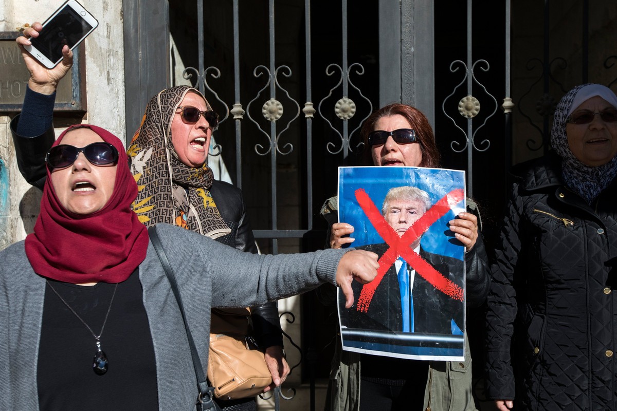 epa06379154 A Palestinian woman hold a poster of US President Donald J. Trump with a large cross through it as another woman gives the thumbs down during running clashes on a central East Jerusalem st ...