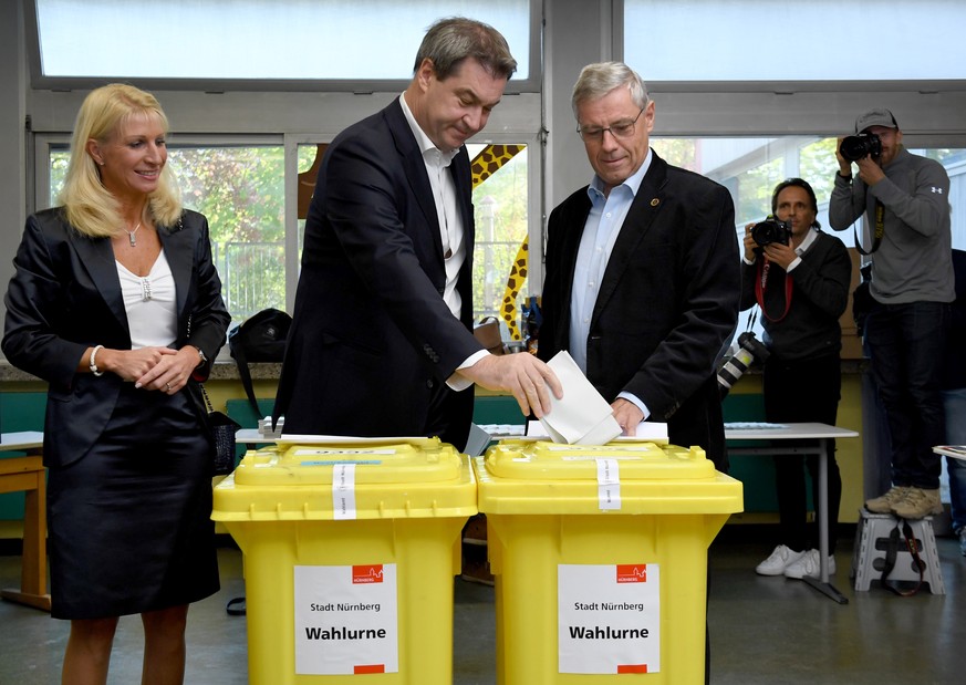 epaselect epa07092066 Bavarian Prime Minister Markus Soeder (C) casts his ballot next to his wife Karin Baumueller (L) during the Bavaria state elections at a polling station in Nuremberg (Nuernberg), ...