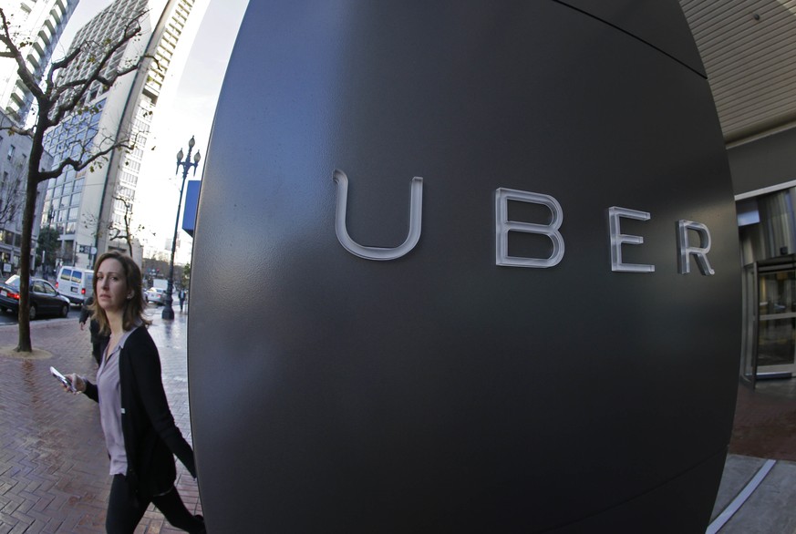 FILE - In this file photo taken Tuesday, Dec. 16, 2014, a woman walks past the company logo of the internet car service, Uber, in San Francisco, USA. A British employment tribunal ruled Friday Oct. 28 ...