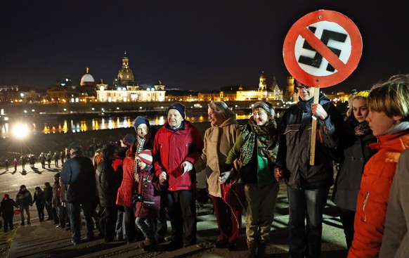 epa04075110 Demonstrators commemorate the destruction of Dresden during the Second World War with a human chain and a sign with a crossed out swastika in Dresden, Germany, 13 February 2014. The singn  ...