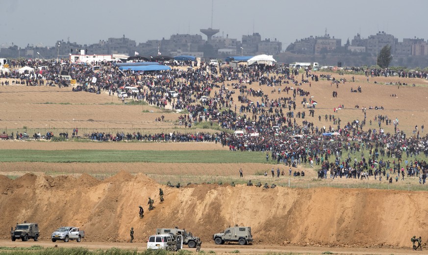 epa06636823 Palestinians gather on the Palestinian side of the border, as Israeli soldiers take position, next to the Gaza town of Beit Hanun, 30 March 2018. The Israeli army is on high alert and depl ...