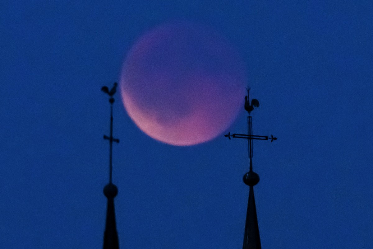 The blood moon rises behind the cross and rooster of two churches steeple during a total lunar eclipse, in Bottens, Switzerland, Sunday, September 7, 2025.(KEYSTONE/Laurent Gillieron)