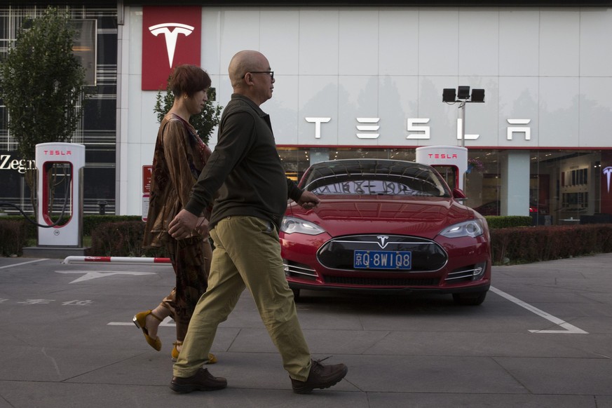 People walk past a Tesla vehicle parked outside a showroom in Beijing, China, Tuesday, May 22, 2018. China said Tuesday it will reduce auto import duties effective July 1 following pledges to buy more ...