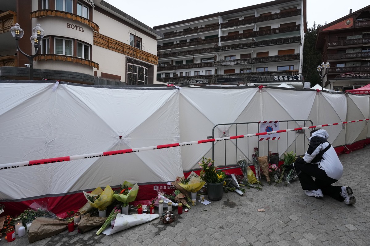 People bring flowers near the sealed off Le Constellation bar in Crans-Montana, Swiss Alps, Switzerland, Friday, Jan. 2, 2026, where a devastating fire left dead and injured during the New Year's ...