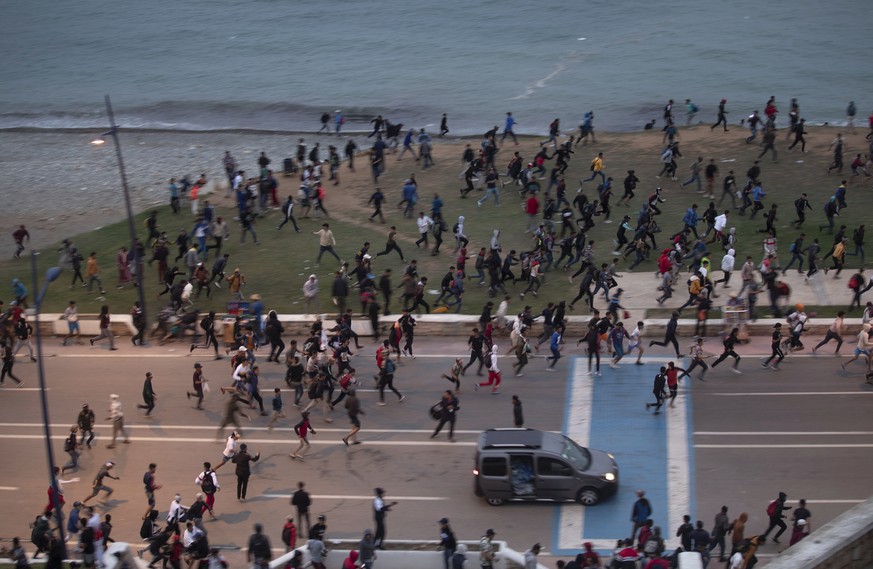 Moroccan youth run for cover as they clash with Moroccan security forces while trying to cross to the Spanish enclave of Ceuta, in Fnideq, Morocco, on Wednesday, May 19, 2021. Spain&#039;s north Afric ...