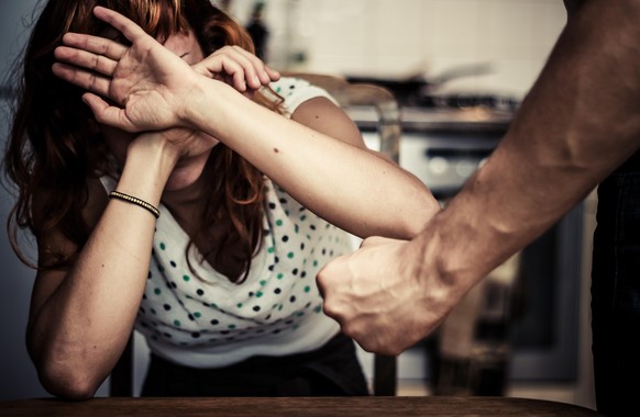 Konzept der häuslichen Gewalt mit verängstigter und verletzter Frau, die vor einem gewalttätigen Mann schützt