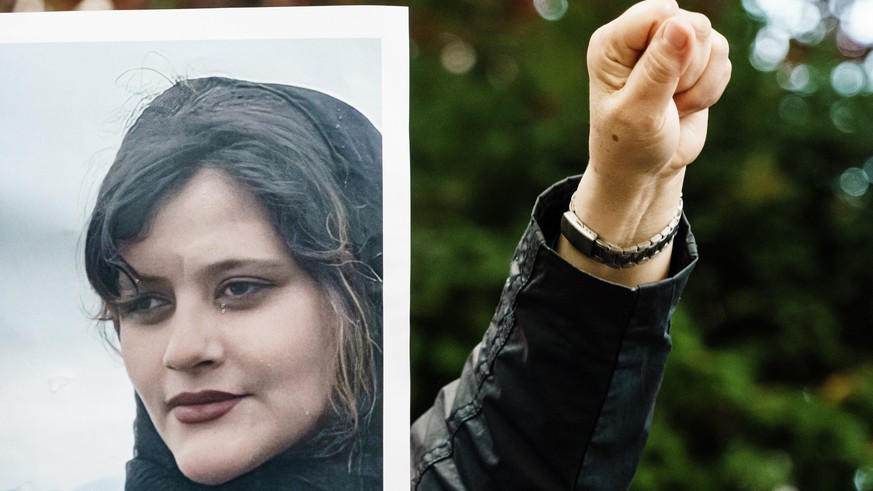 epa10195345 A protester of the National Council of Resistance of Iran (NWRI) gestures during a demonstration with her fist, while being covered by a placard, showing deceased Mahsa Amini, in front of  ...