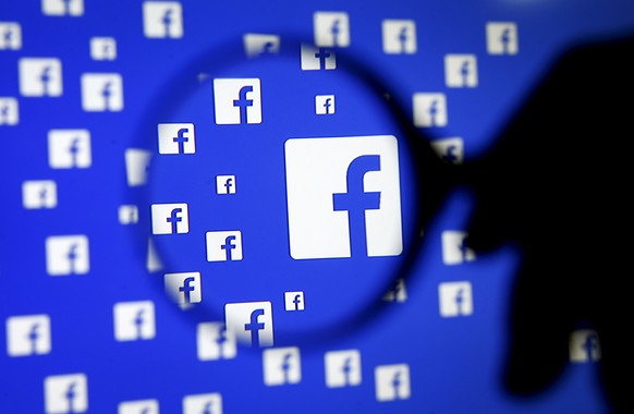 A man poses with a magnifier in front of a Facebook logo on display in this illustration taken in Sarajevo, Bosnia and Herzegovina, December 16, 2015. REUTERS/Dado Ruvic/File Photo