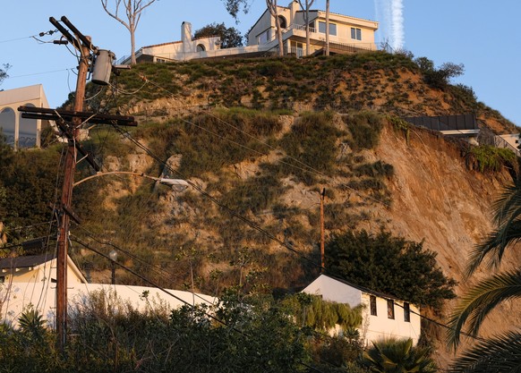 A broken utility poll remains standing, left, as a deck of a home, right, juts out precariously over an area where a landslide occurred in the Hollywood Hills area of Los Angeles on Tuesday, Jan. 31,  ...