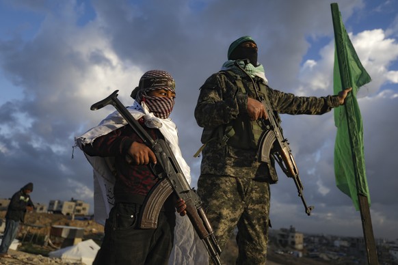 A boy holds a weapon as he stands next to a Hamas fighter standing in position ahead of the militant group handing over four bodies to the Red Cross in Khan Younis, southern Gaza Strip, Thursday, Feb. ...