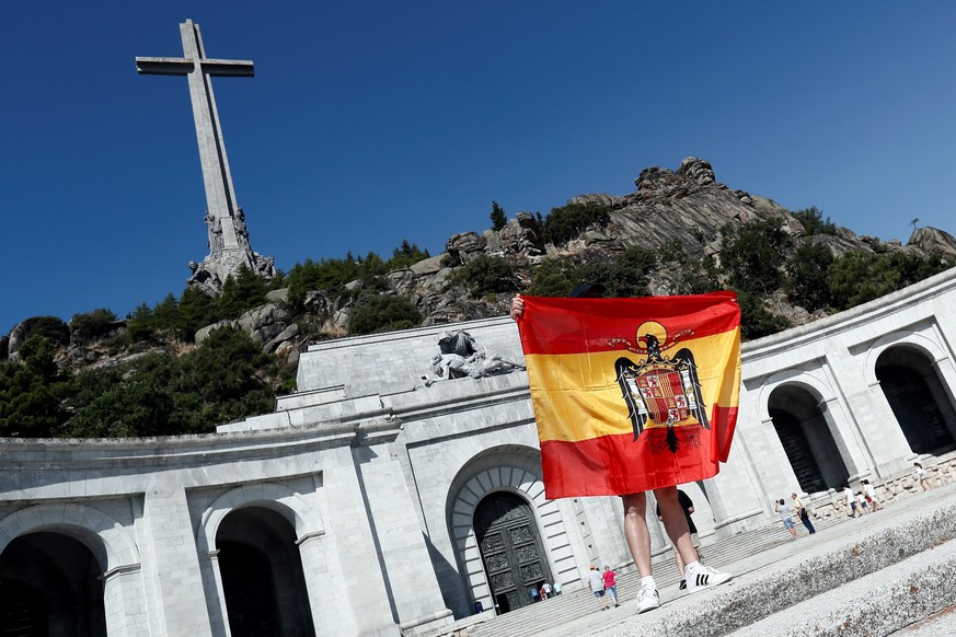 epa06962491 A person holds a Franco era Spanish flag on the esplanade of the El Valle de los Caidos (The Valley of the Fallen) memorial complex in the town of San Lorenzo del Escorial, 40 kilometers f ...