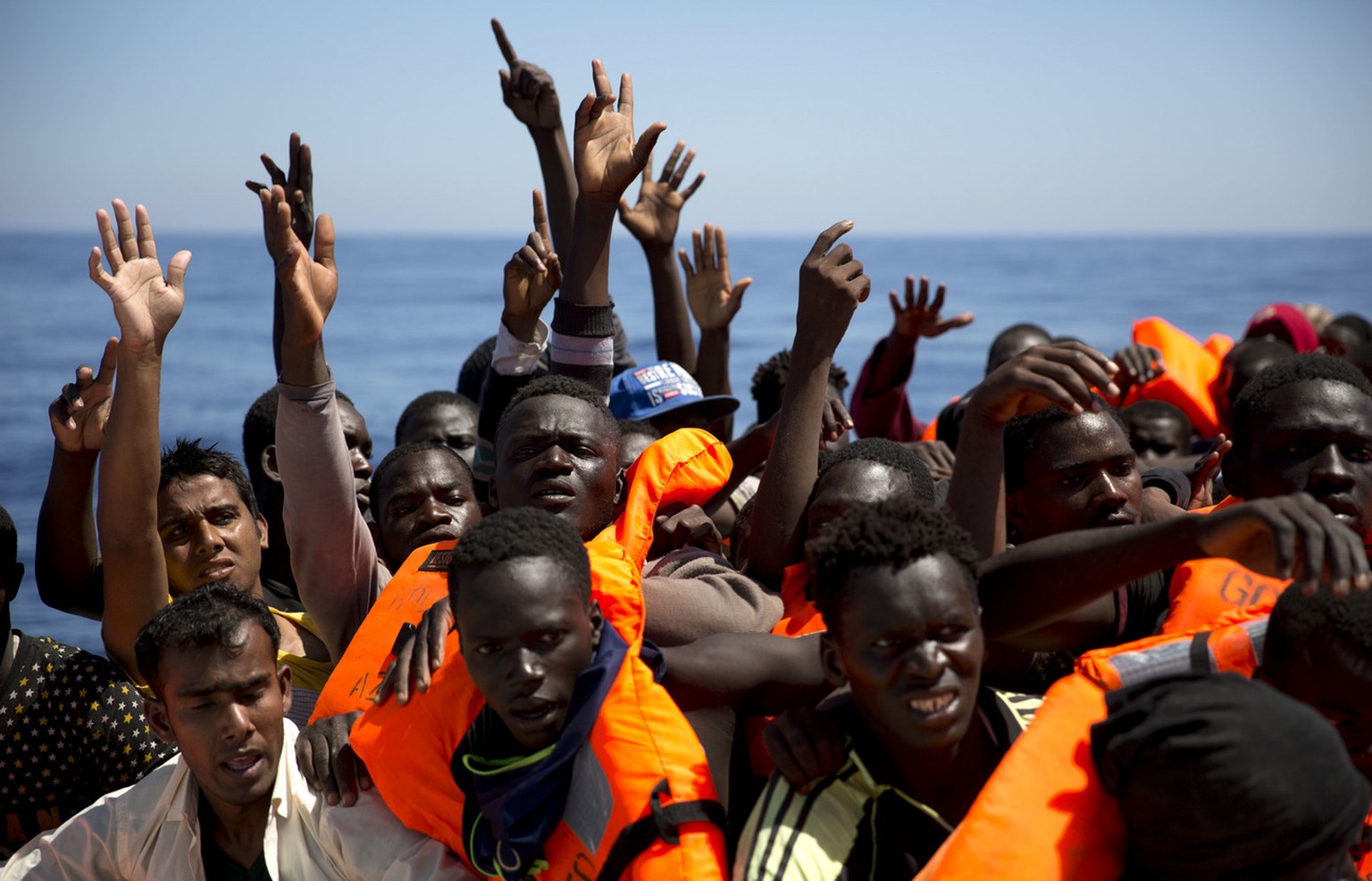 Migrants and refugees raise their hands as they try to reach life vests distributed by Spanish NGO Proactiva Open Arms workers, after being located out of control sailing on a rubber boat in the Medit ...