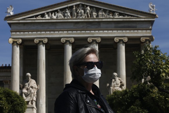 epa08293903 A woman wearing a mask waits for a bus as he stands in front of the Athens Academy building in central Athens, Greece, 14 March 2020. Greece expanded its measures of closures on Friday 13  ...