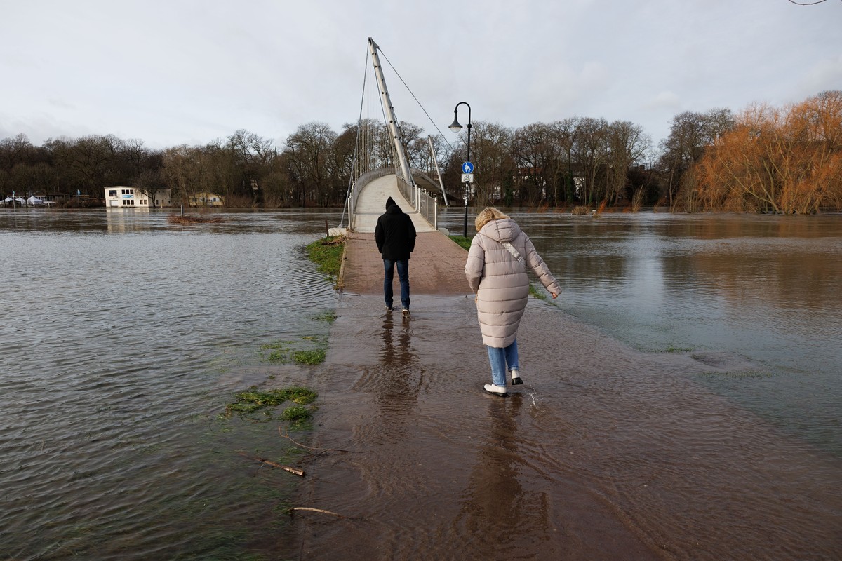 30.12.2023, Nordrhein-Westfalen, Minden: Spazierg�nger betreten eine Br�cke �ber den Hochwasser f�hrenden Flu� Weser. Trotz leichter Entspannung der Pegelst�nde f�hren zahlreiche B�che und Fl�sse in N ...
