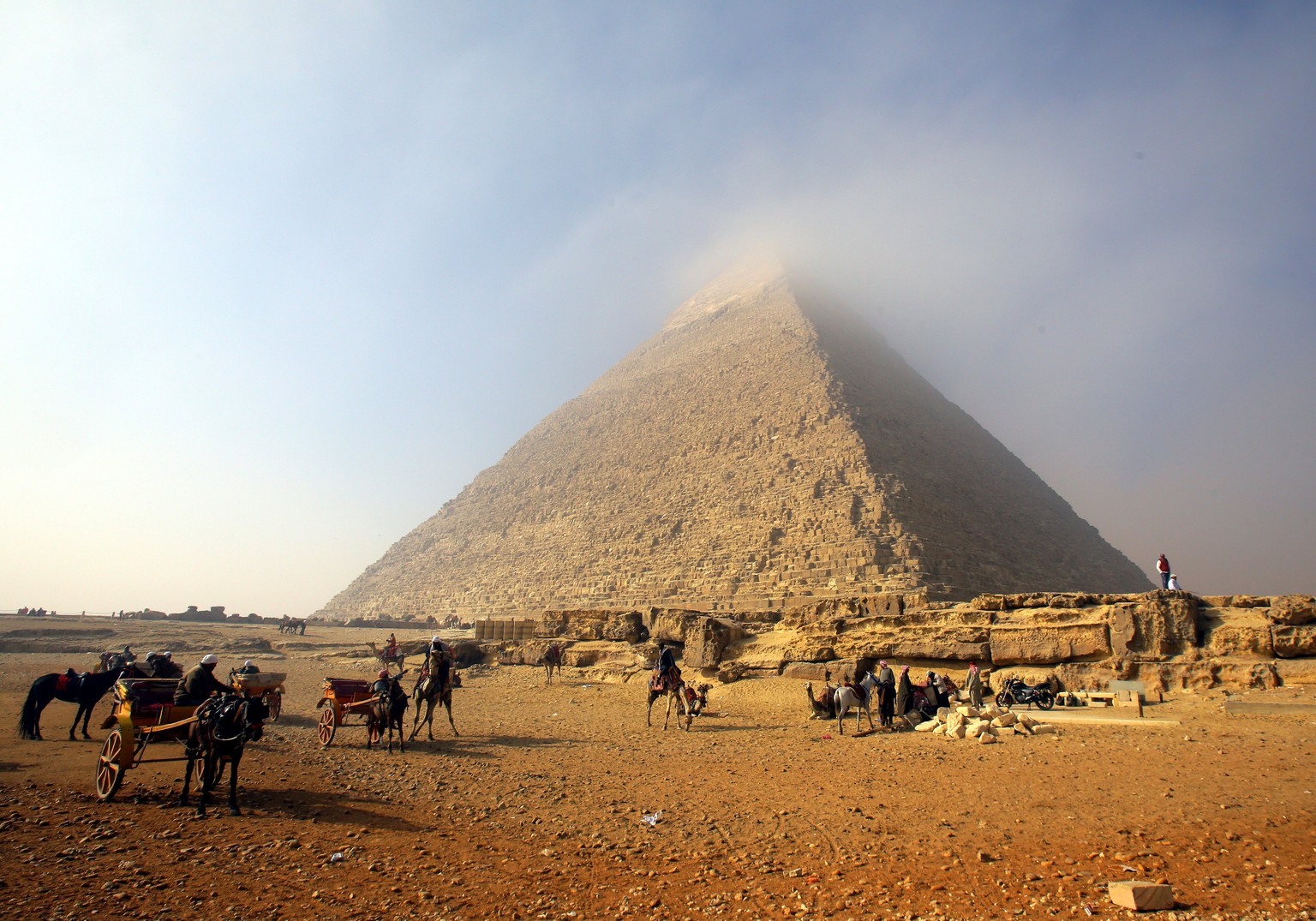 epaselect epa06493728 Camel riders wait for tourists as a mist cloud covers the apex of the Pyramid of Cheops (Khufu), the biggest of the three Giza Pyramids, in Giza, on the southern outskirts of Cai ...
