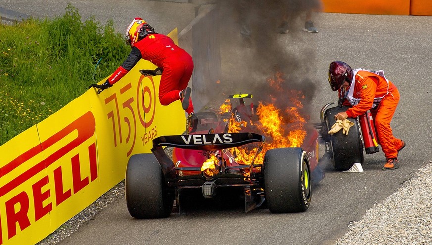 Während Sainz aus dem brennenden Ferrari springt, versucht ein Marshal das Rad zu blockieren.