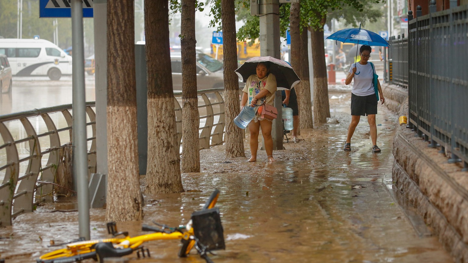 epa10779177 A woman carries a water container along a muddy road during a downpour in Mentougou District, west of Beijing, China, 01 August 2023. Heavy rains brought by Typhoon Doksuri caused floods i ...