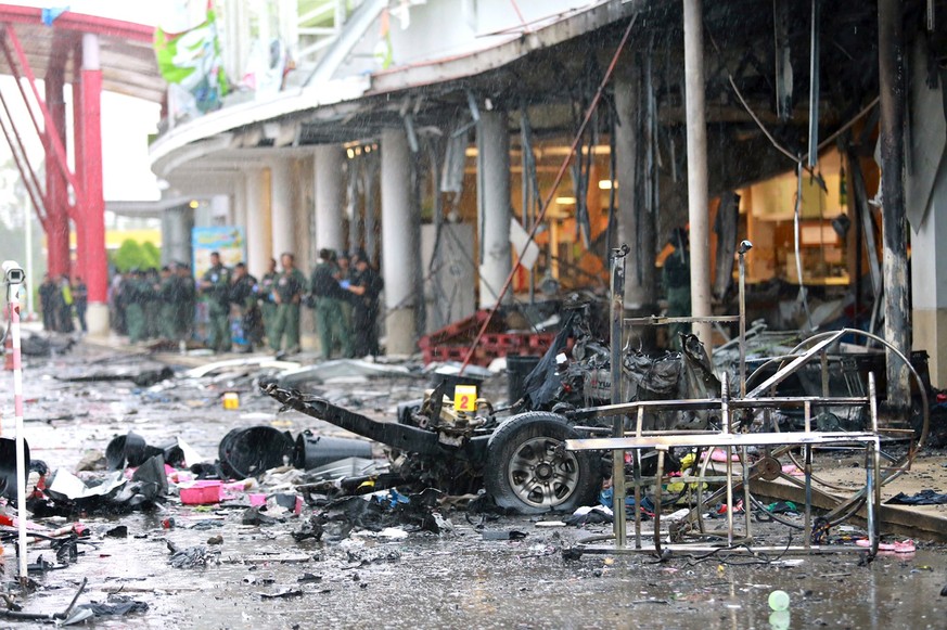 epa05952123 Thai Explosive Ordnance Disposal officers (back) walk near bomb damaged vehicles following a car bomb at Big C supermarket in Pattani province, southern Thailand, 09 May 2017. At least 52  ...