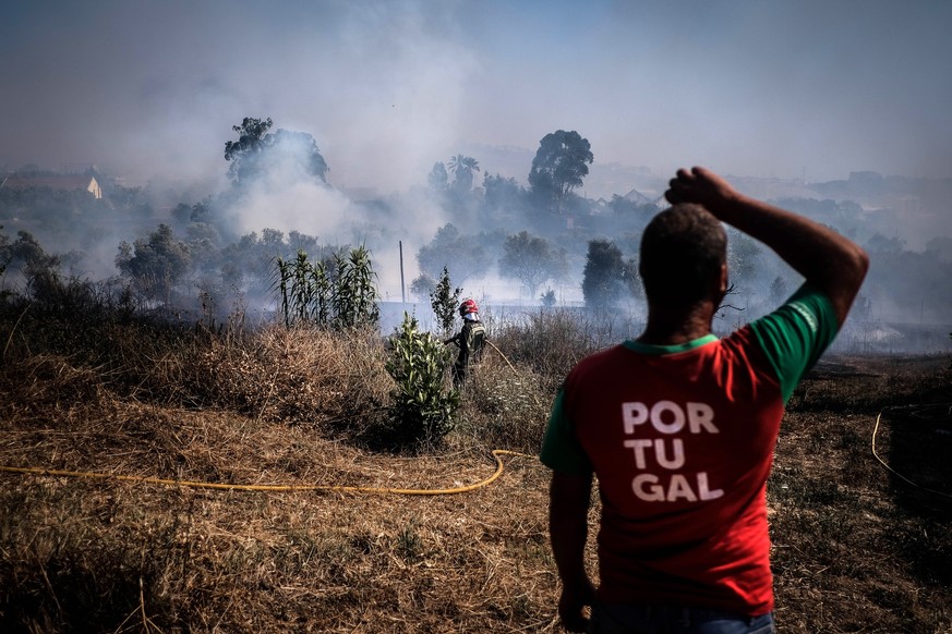 epa10064085 A man stands as a firefighter works near a burning area during a forest fire in Canecas, outskirts of Lisbon, Portugal, 10 July 2022. Portugal&#039;s President warned that the risk of fire ...