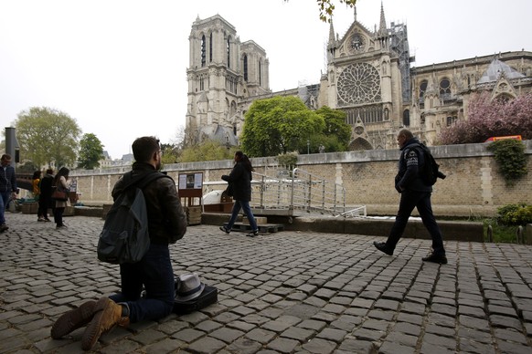 Man kneels as people came to watch and photograph the Notre Dame cathedral after the fire in Paris, Tuesday, April 16, 2019. Experts are assessing the blackened shell of Paris' iconic Notre Dame cathedral to establish next steps to save what remains after a devastating fire destroyed much of the almost 900-year-old building. With the fire that broke out Monday evening and quickly consumed the cathedral now under control, attention is turning to ensuring the structural integrity of the remaining building. (AP Photo/Christophe Ena)