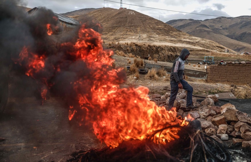 epa10394492 A man passes a burning barricade as the community of La Estrella between Cusco and Juliaca block the roads in the vicinity of the Juliaca airport in Juliaca, Peru, 07 January 2022. Protest ...