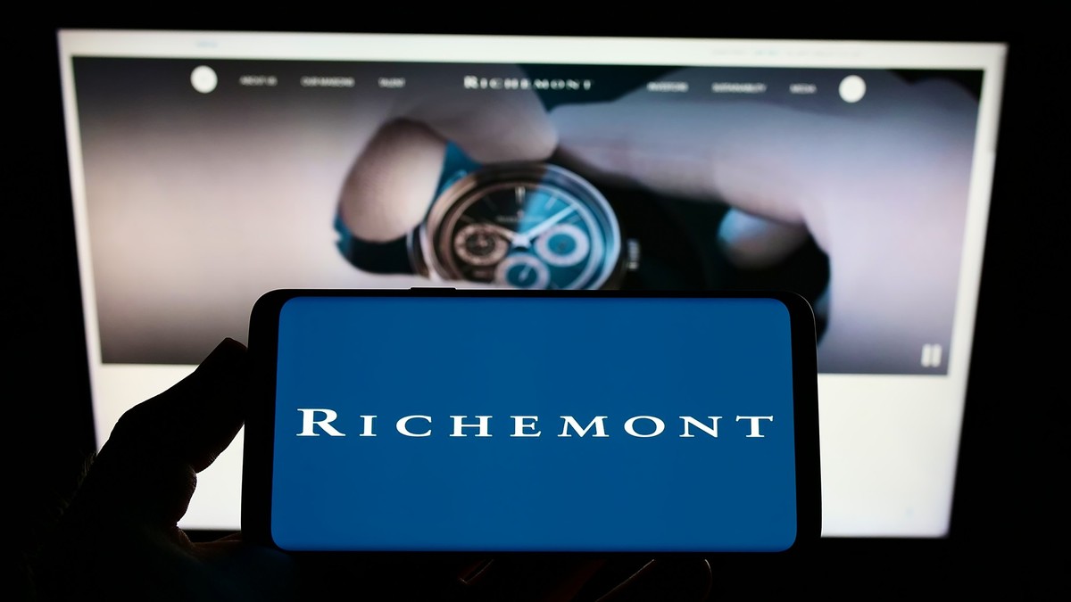Person holding smartphone with logo of Swiss company Compagnie Financiere Richemont S.A. on screen in front of website. Focus on phone display. *** Person haltend smartphone mit Schriftzug des Schweiz ...