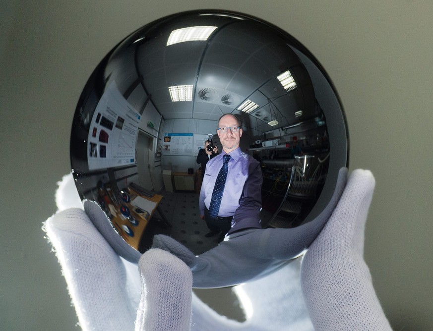 epa04491665 A picture made available on 16 November 2014 shows Scientist Arnold Nicolaus holding a silicon sphere which weighs exactly one kilogram as he is reflected on it, at the Physikalisch-Techni ...