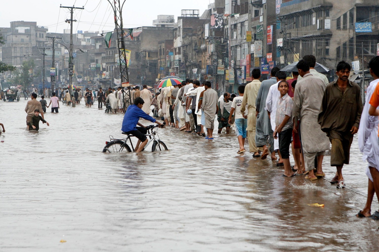 People walk in a queue on a road submerged in water after heavy rainfall in Lahore, Pakistan, Friday, June 29, 2007. The widespread flooding struck in the wake of a cyclone that dumped torrential rain ...