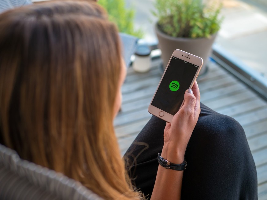 Stockholm, Sweden - June 14, 2018: Women holding a smartphone or cellphone with Spotify music app loading. View from back, selective focus.
