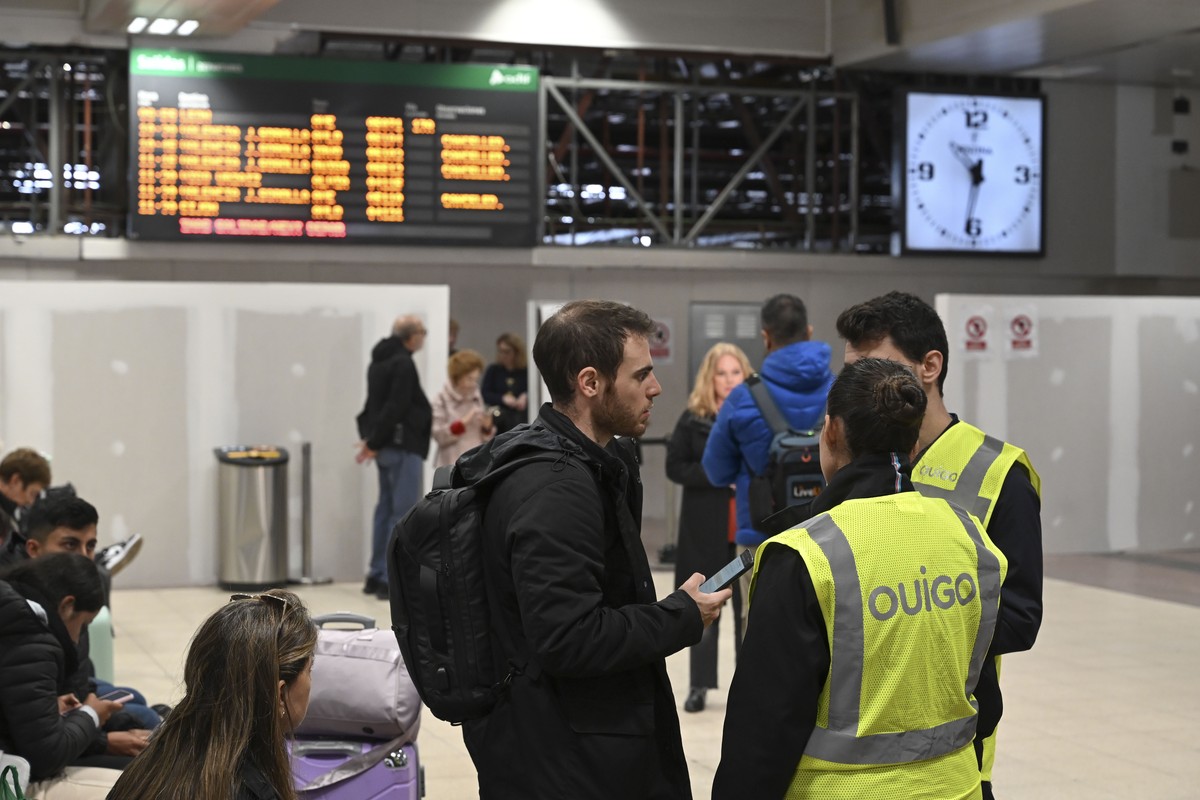 epa11692104 A traveler speaks with two employees of the Ouigo low-cost train service in front of information screens displaying the cancellation of train services between Madrid and Valencia at Chamar ...
