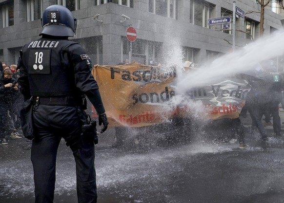 epa08820521 A police water cannon fires against left-wing protesters who try to stop a demonstration against the coronavirus restrictions, in Frankfurt am Main, Germany, 14 November 2020. The protests ...