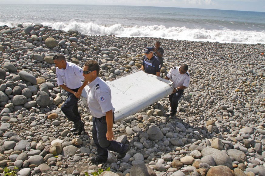 In this photo dated Wednesday, July 29, 2015, French police officers carry a piece of debris from a plane in Saint-Andre, Reunion Island. Air safety investigators, one of them a Boeing investigator, h ...