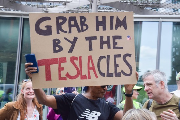 June 14, 2025, London, England, United Kingdom: A protester holds a Grab him by the Tesla-cles sign during the No Tyrants protest outside the Embassy of USA , part of the anti-Trump No Kings mass prot ...