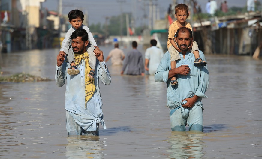 epa10145316 People carrying children wade through a flooded area following heavy rains in Nowshera District, Khyber Pakhtunkhwa province, Pakistan, 29 August 2022. According to the National Disaster M ...