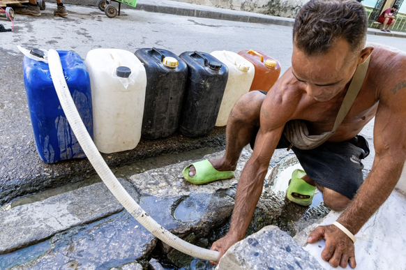 Alltag in der Krise: Ein Mann zapft sich per Schlauch Wasser aus einer unterirdischen Leitung ab.