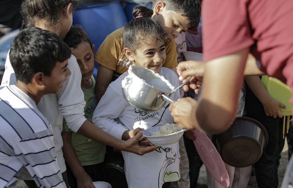 epa10938583 Palestinian children receive food between tents set up for Palestinians seeking refuge on the grounds of a United Nations Relief and Works Agency for Palestine Refugees (UNRWA) center in K ...