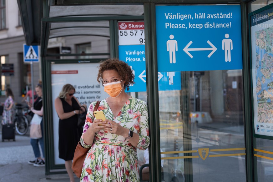 epa08510994 A woman wearing a face mask stands at a bus stop featuring a sign reminding passengers to maintain a minimum social distance between each other to reduce the risk of infection with the SAR ...