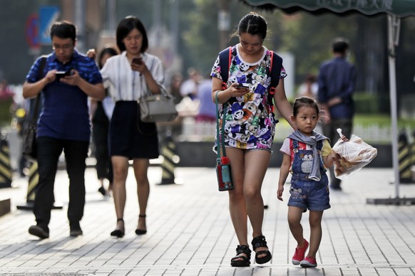 Pedestrians view their smartphones as they walk along a sidewalk in Beijing, Wednesday, Aug. 9, 2017. China has one of the world's largest mobile phone market and become more and more popular among al ...