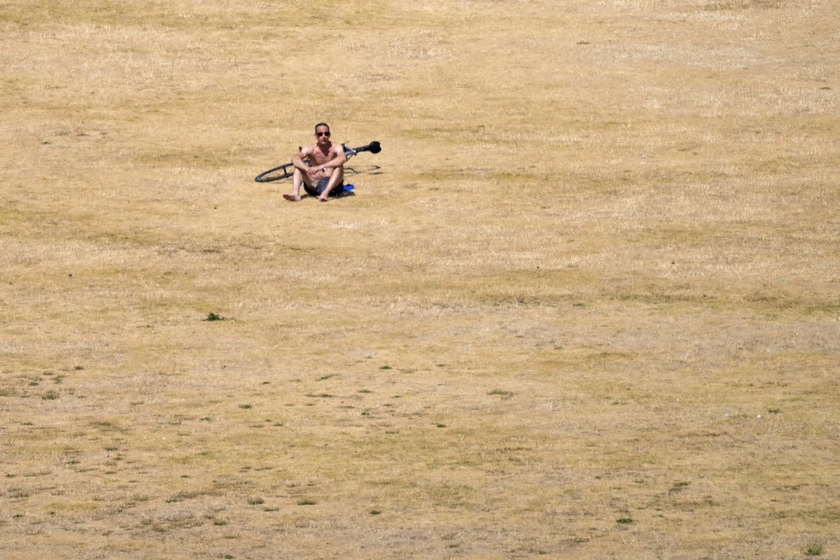 A cyclist sits on the dry grass of Greenwich Park, in south east London, Monday July 18, 2022. Britain���s first-ever extreme heat warning is in effect for large parts of England as authorities prepar ...