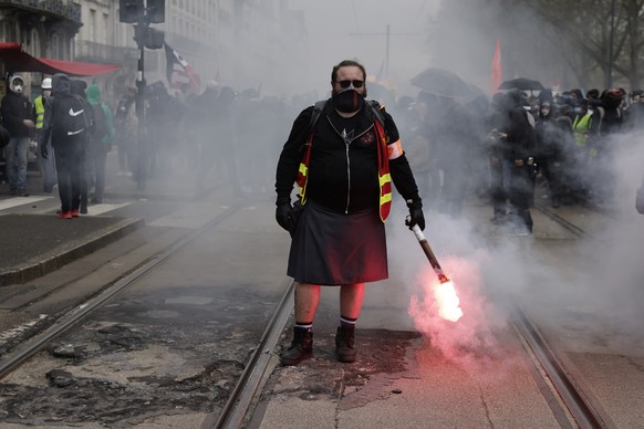 A demonstrator holds a flare during a protest Thursday, April 6, 2023 in Nantes, western France. Hundreds of thousands of people are expected to fill the streets of France Thursday for the 11th day of ...